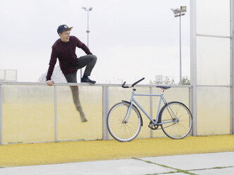 Urban cyclist climbing over fence on sports field - CUF29978
