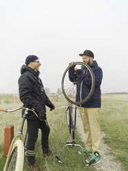 Urban cyclists fixing tyre in field - CUF29982