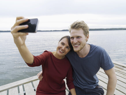 Paar auf dem Pier nebeneinander mit Smartphone, um lächelnd ein Selfie zu machen, Kopenhagen, Dänemark - CUF29987