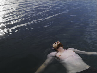 High angle view of young man floating on back in water arms outstretched looking up - CUF29989