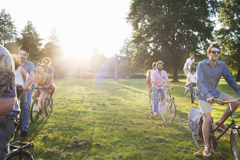 Reihen von feiernden Erwachsenen, die bei Sonnenuntergang auf Fahrrädern im Park ankommen - CUF29997