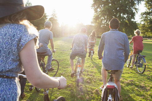 Rückansicht einer Gruppe Erwachsener, die bei Sonnenuntergang auf Fahrrädern im Park ankommt - CUF30000