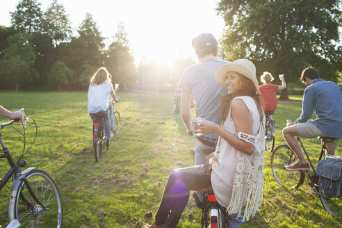 Rear view of party going adults in park on bicycles at sunset - CUF30001
