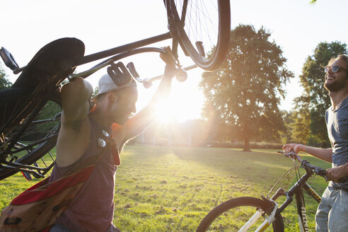 Zwei männliche Freunde kommen bei Sonnenuntergang mit Fahrrädern im Park an - CUF30002
