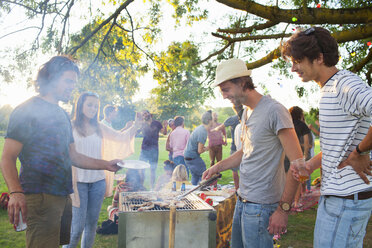 Happy adult friends barbecuing at sunset party in park - CUF30009