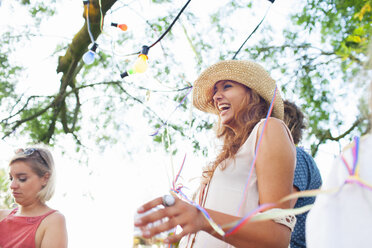 Young adult friends wrapped in streamers at sunset party in park - CUF30014