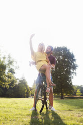 Young couple on bicycle taking smartphone selfie in sunlit park - CUF30022