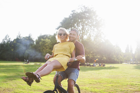 Porträt eines jungen Paares, das sich bei Sonnenuntergang im Park auf dem Fahrrad amüsiert - CUF30024