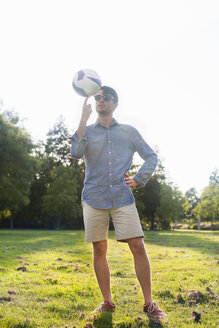 Porträt eines jungen Mannes beim Drehen eines Balls in einem sonnenbeschienenen Park - CUF30026
