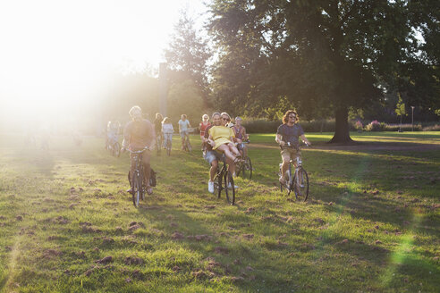 Scharen erwachsener Freunde, die auf Fahrrädern zur Party im Park bei Sonnenuntergang ankommen - CUF30033