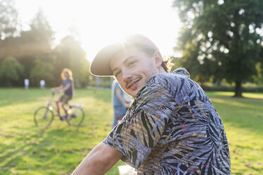 Porträt eines jungen Mannes, der im sonnenbeschienenen Park über seine Schulter schaut - CUF30035