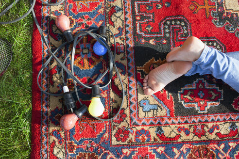 Draufsicht auf nackte Füße einer Frau und dekorative Lichter auf einem Teppich im Park - CUF30039