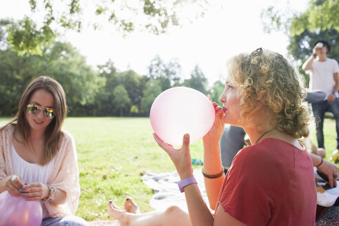Junge Frau bläst Luftballon im Park auf - CUF30043