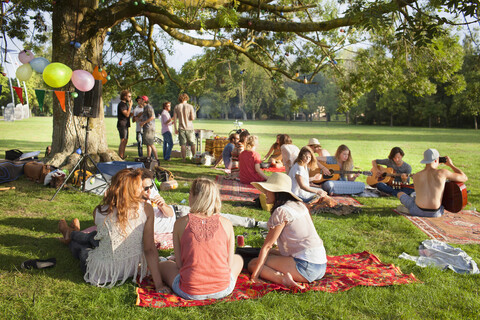 Gruppe von Freunden, die bei Sonnenuntergang unter einem Parkbaum Musik hören, lizenzfreies Stockfoto