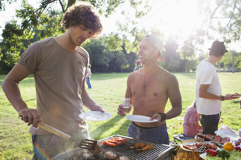 Junge Männer beim Grillen im Park bei Sonnenuntergang, lizenzfreies Stockfoto