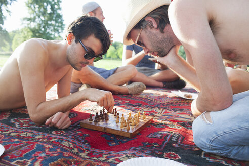 Zwei junge Männer spielen ein Brettspiel bei Sonnenuntergang im Park - CUF30065