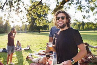 Porträt eines jungen Mannes, der bei einem Gruppenpicknick im Park Bier trinkt - CUF30067