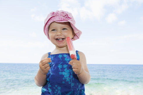 Weibliches Kleinkind mit Sonnenhut isst einen Eislutscher am Strand - CUF30109