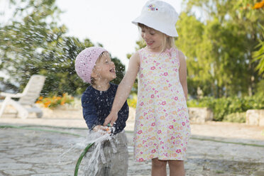 Girl and toddler sister playing with water hosepipe in garden - CUF30112