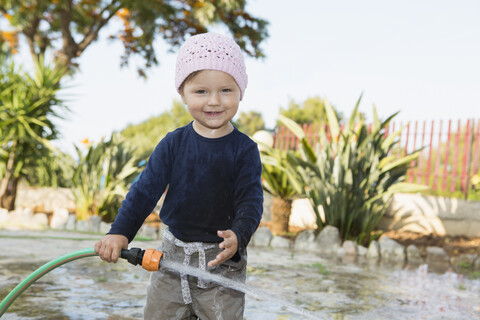 Weibliches Kleinkind spielt mit Wasserschlauch im Garten, lizenzfreies Stockfoto