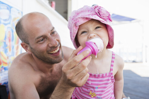 Vater füttert seine kleine Tochter am Strand mit einer Eiswaffel - CUF30116
