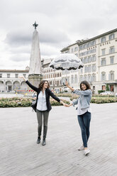 Lesbisches Paar mit Regenschirm, das sich lächelnd an den Händen hält, Piazza Santa Maria Novella, Florenz, Toskana, Italien - CUF30154