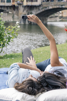 Lesbisches Paar, das sich hinlegt und ein Smartphone benutzt, um ein Selfie vor der Ponte Vecchio über dem Fluss Arno zu machen, Florenz, Toskana, Italien - CUF30168