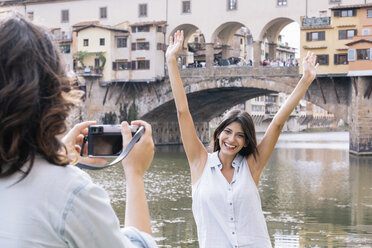 Young woman arms raised posing for photograph in front of Ponte Vecchio and river Arno, Florence, Tuscany, Italy - CUF30171