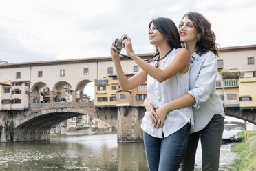 Lesbisches Paar, das sich vor der Ponte Vecchio und dem Fluss Arno umarmt und eine Digitalkamera zum Fotografieren benutzt, Florenz, Toskana, Italien - CUF30173