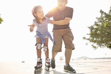 Älterer Mann unterstützt Tochter beim Rollerbladen am Strand, Zhuhai, Guangdong, China - CUF30231