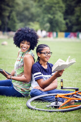 Boy and mother back to back in park reading book - CUF30238