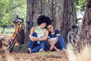 Mature woman and son sitting against park tree - CUF30241