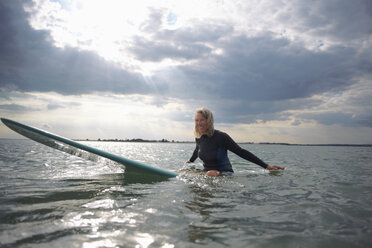 Portrait of senior woman sitting on surfboard in sea, smiling - CUF30256