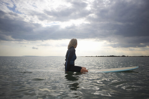 Ältere Frau sitzt auf einem Surfbrett im Meer, Rückansicht, lizenzfreies Stockfoto