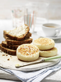 Crumpets und Vollkornbrot mit Butter auf einem alten Schneidebrett mit einer Tasse Tee - CUF30281