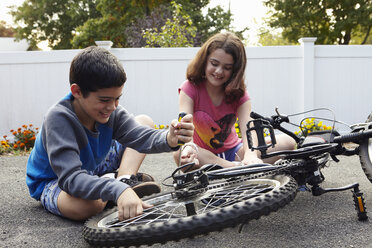Bruder und Schwester reparieren Fahrrad in der Einfahrt - ISF09590