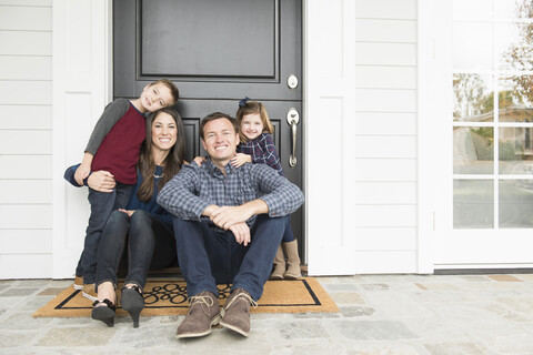 Porträt von Eltern und zwei Kindern an der Haustür sitzend, lizenzfreies Stockfoto