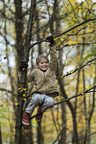 Mädchen hält sich an einem Ast im Herbstwald fest, lizenzfreies Stockfoto