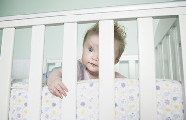 Portrait of baby girl looking through bars on cot - CUF30644