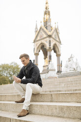 Junger Mann sitzt auf den Stufen und liest Smartphone-Texte, Albert Memorial, London, England, UK - CUF30768