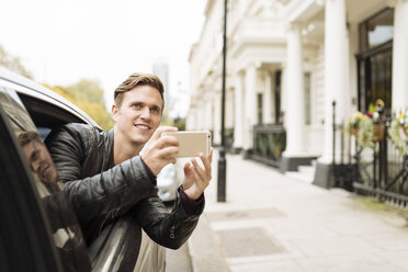 Young man taking photographs from car window, London, England, UK - CUF30774