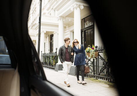 Blick aus dem Autofenster auf ein junges Paar, das auf der Straße spazieren geht, London, England, UK - CUF30775