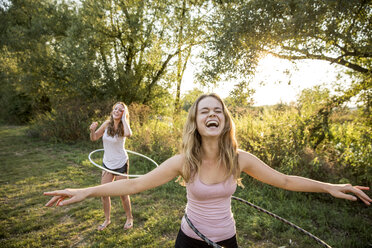 Zwei junge Mädchen in ländlicher Umgebung, die mit Hula-Hoop-Reifen herumalbern, - CUF30841