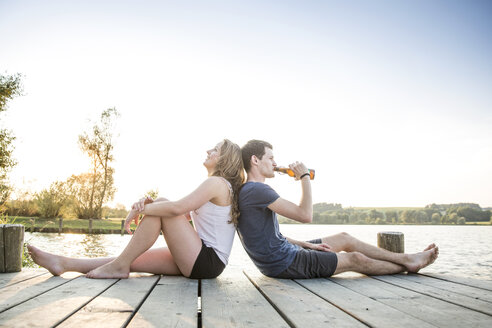 Young couple relaxing on jetty, sitting back to back - CUF30845