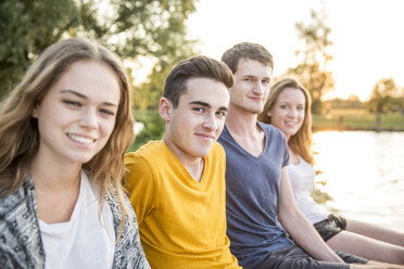 Portrait of group of friends sitting beside lake, smiling - CUF30849