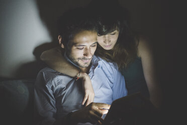 Junge Frau sitzt mit einem Arm um einen jungen Mann, der von einem Laptop-Bildschirm beleuchtet wird - CUF30853