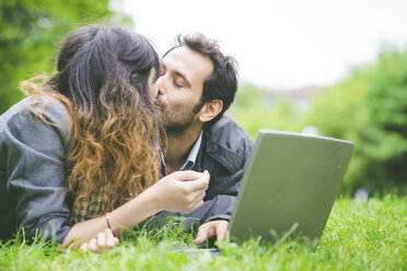 Head and shoulders of young couple lying on front on grass with laptop computer smiling - CUF30855