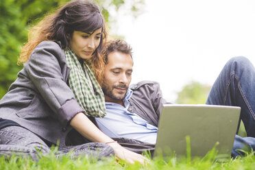 Young couple sitting on grass looking down using laptop computer - CUF30859