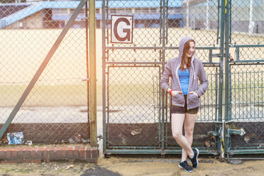 Young woman standing beside sports ground, London, UK - CUF30867