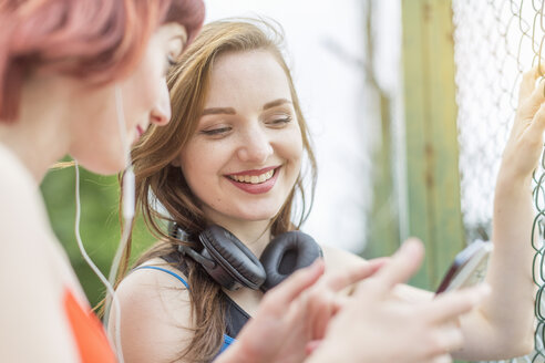 Junge Frauen benutzen ihr Smartphone neben dem Zaun - CUF30872